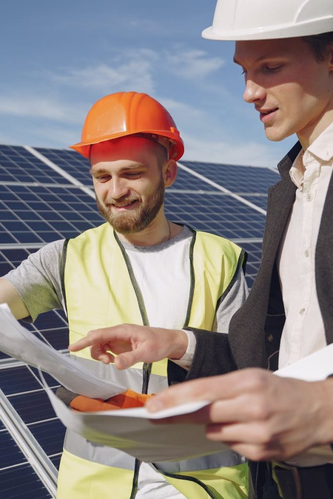 Two engineers reviewing plans for solar panel installation, representing teamwork in renewable energy.